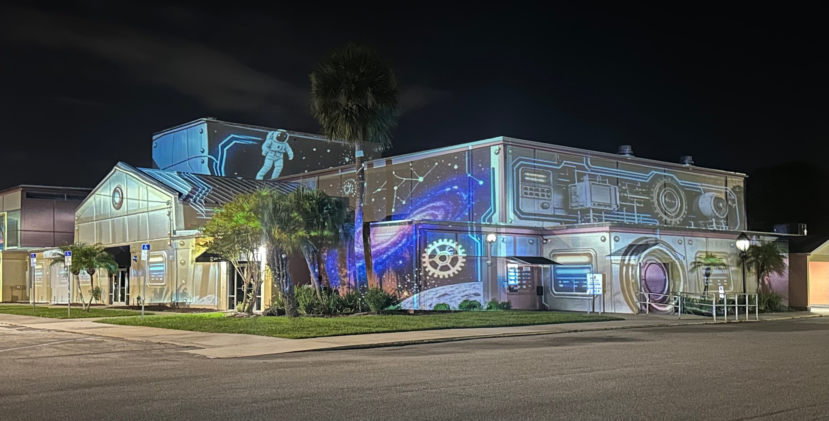 Space-themed projection mapping with astronaut and galaxy artwork covering a building at night